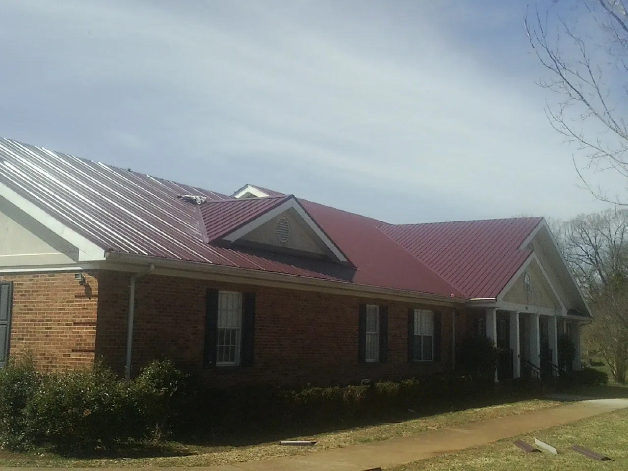 Red metal roof with gabled entries on a long brick building, from a Hail Damage Roof Repair job in Felton