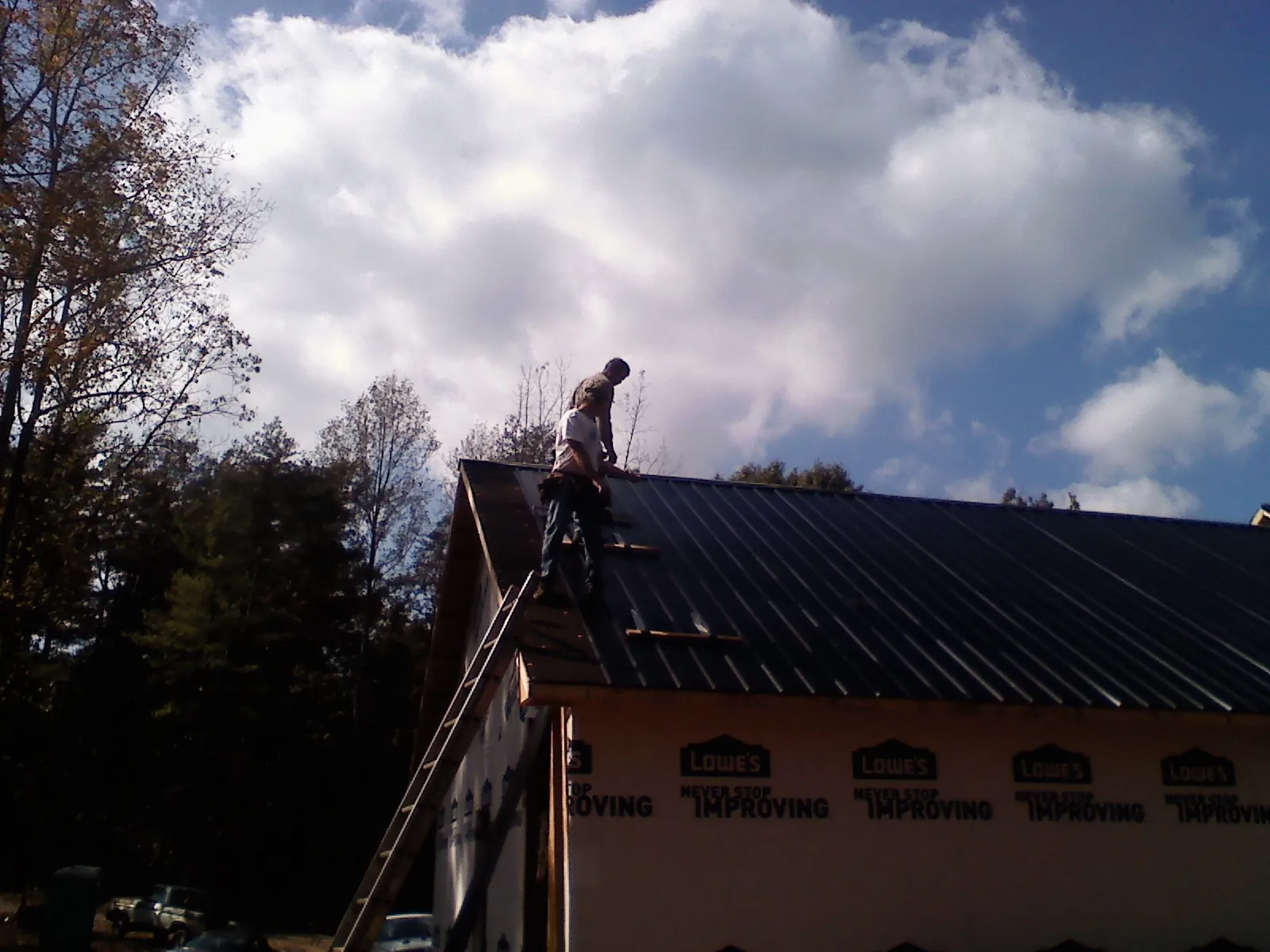 Roofer fastening dark metal panels high against a cloudy sky, from a Roof Inspection job in Felton